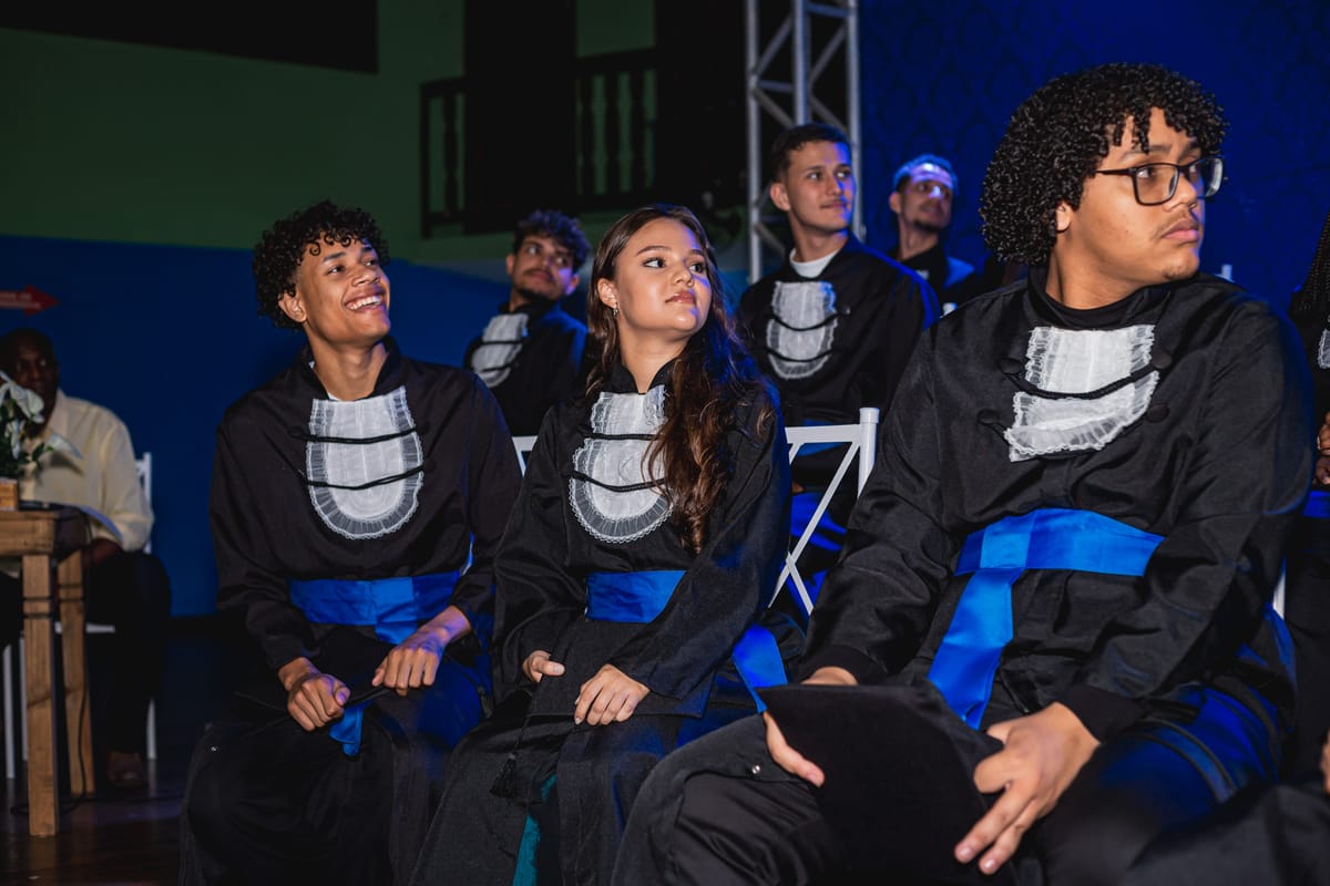 Formandos sentados diante do palco iluminado de azul, durante a cerimônia