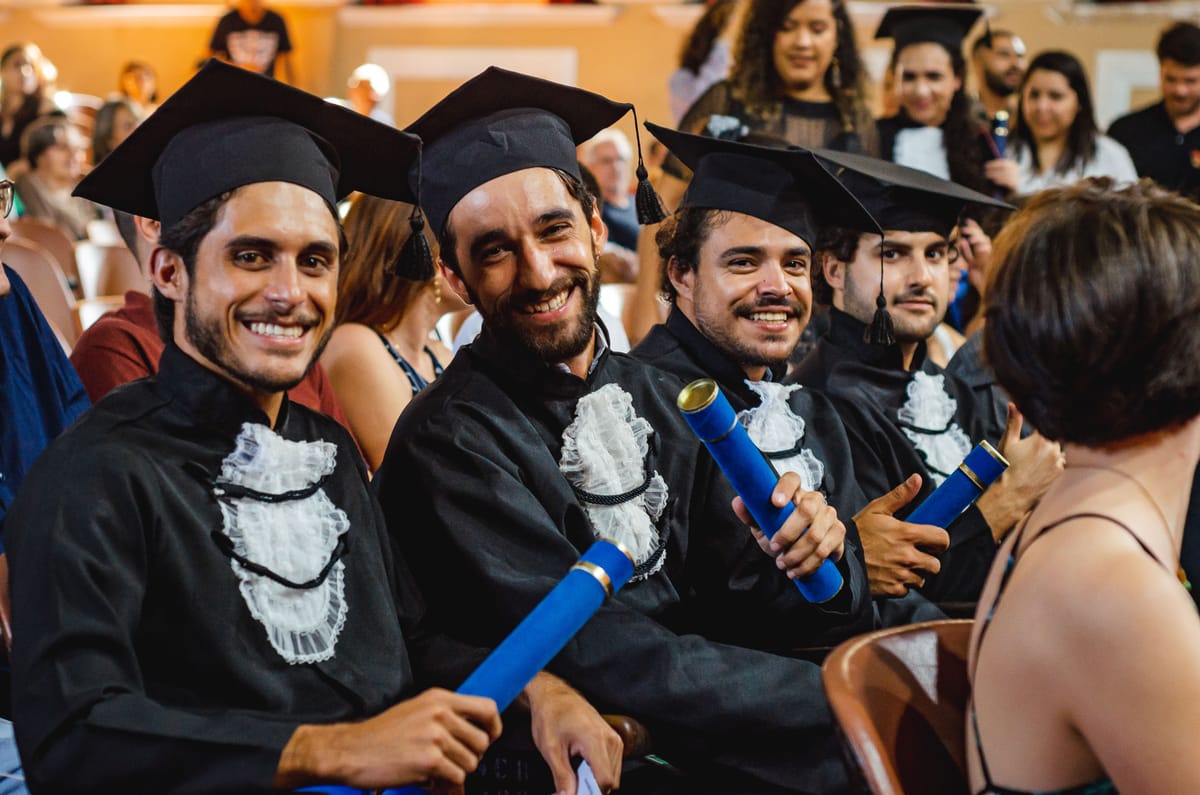 Formandos sentados na cerimônia, sorrindo para a câmera