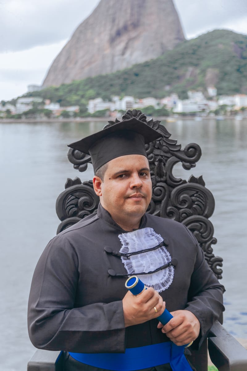 Formando na cadeira de formatura, com o Pão de Açúcar ao fundo