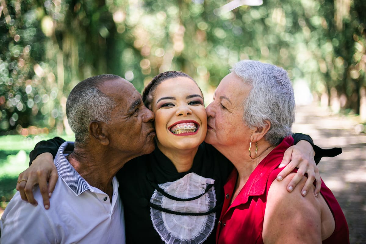 Formanda recebendo beijo de dois familiares mais velhos