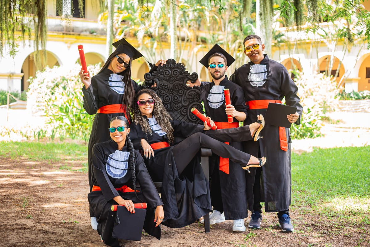Grupo de amigos de beca em volta da cadeira de formatura
