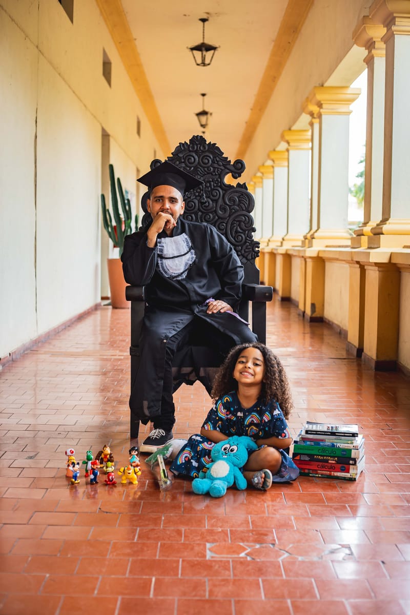 Formando na cadeira no corredor de arcos, com uma criança brincando no chão