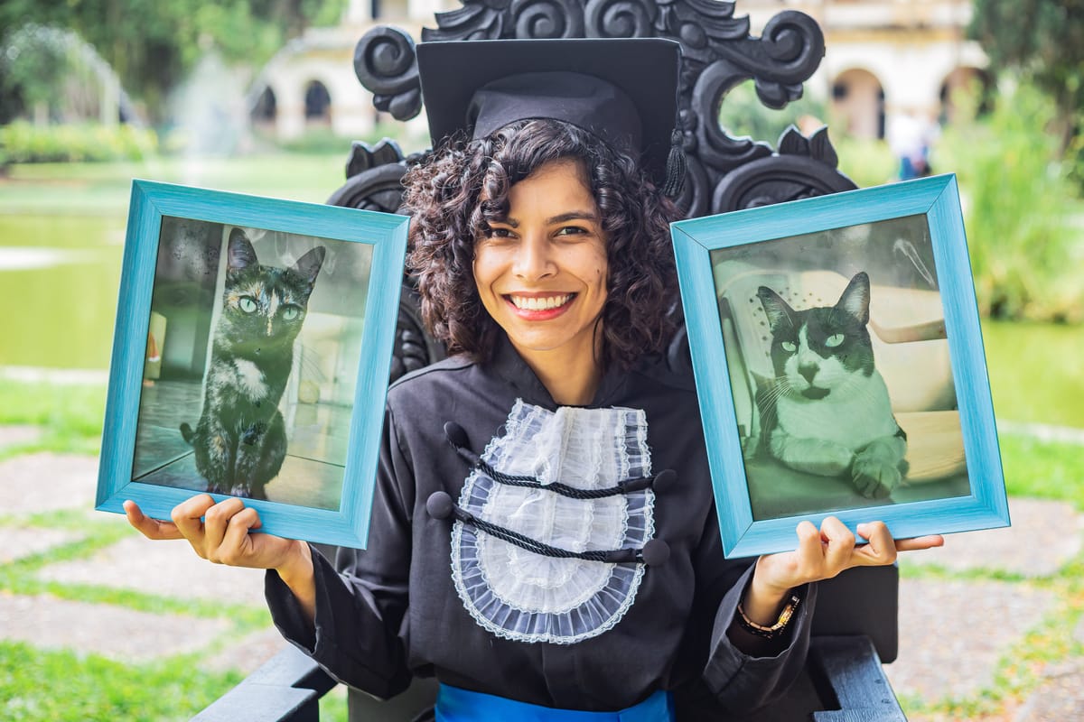 Formanda na cadeira segurando dois quadros com fotos dos seus gatos