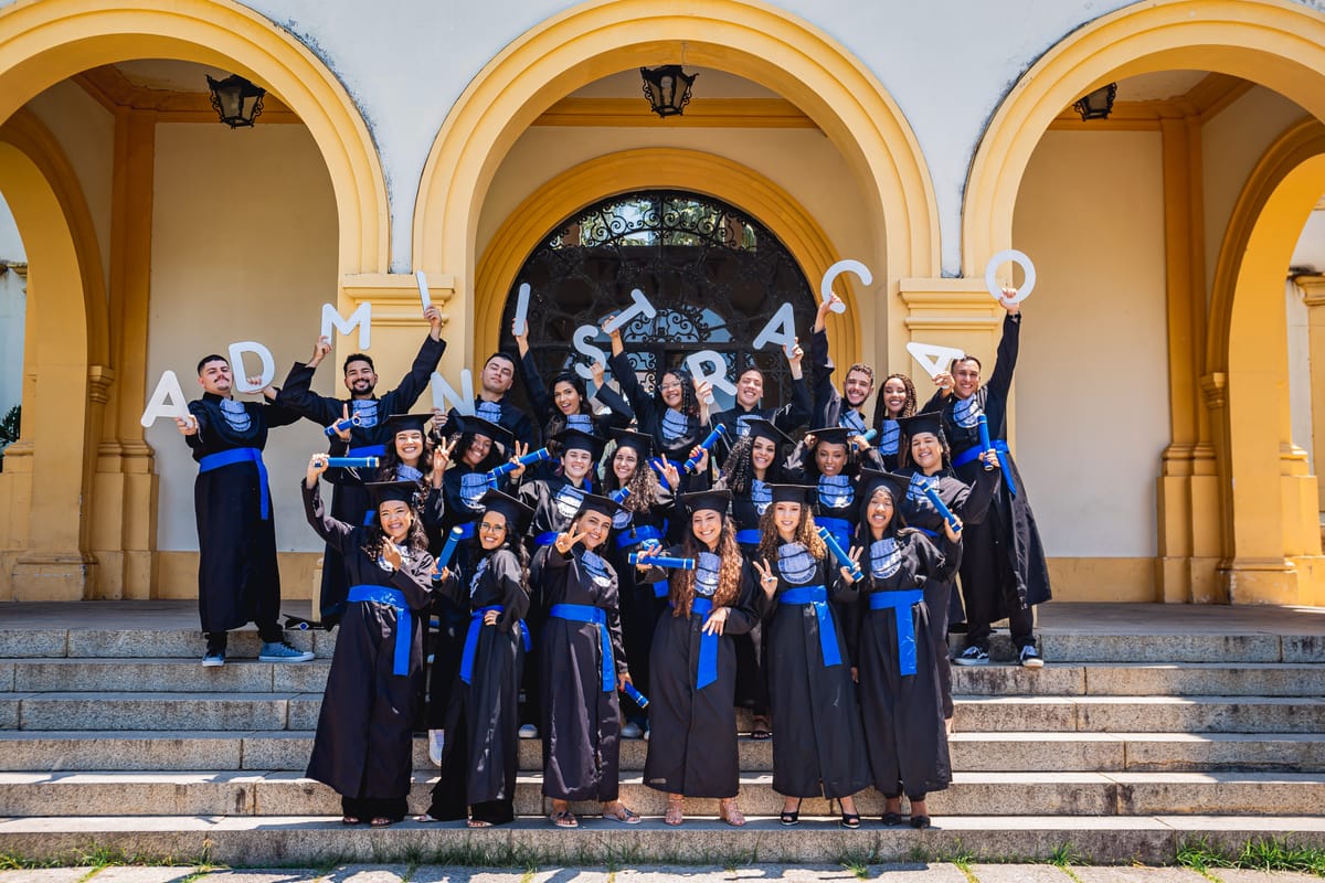 Turma de beca na escadaria do prédio principal, com balões