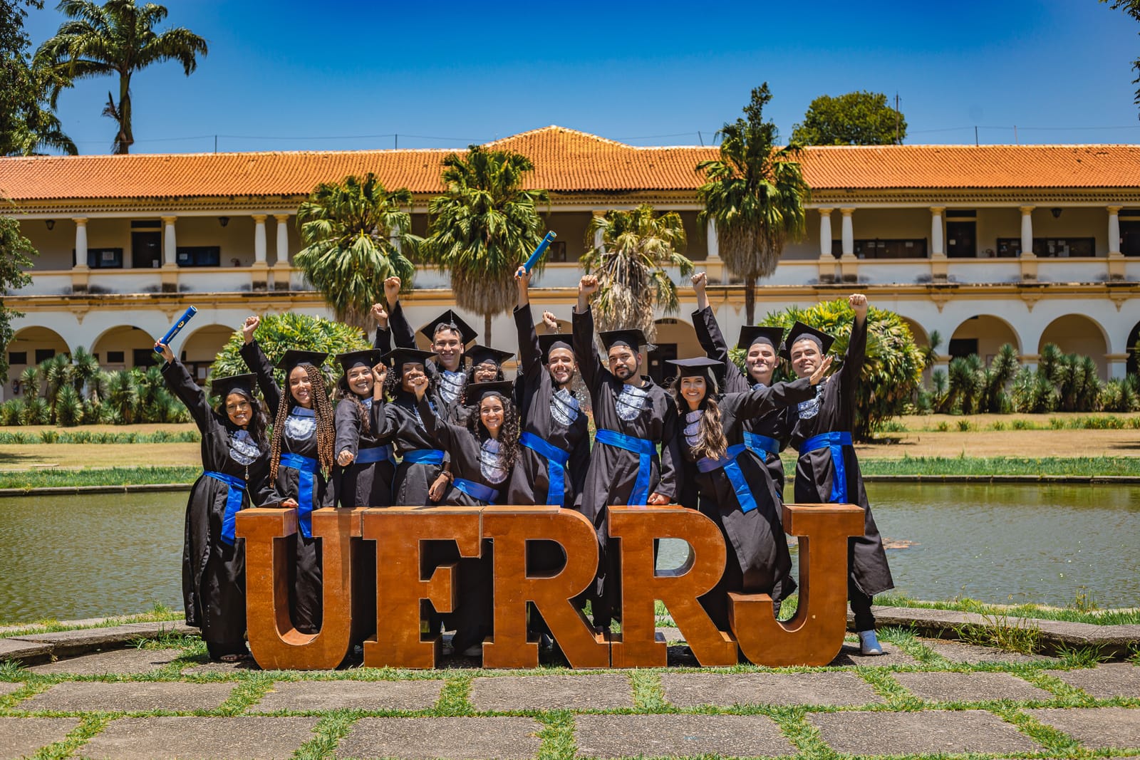 Turma grande de beca atrás das letras da UFRRJ